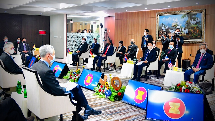 You view a group of men in suits sitting on white armchairs spread around a string of screens showing the ASEAN logo.